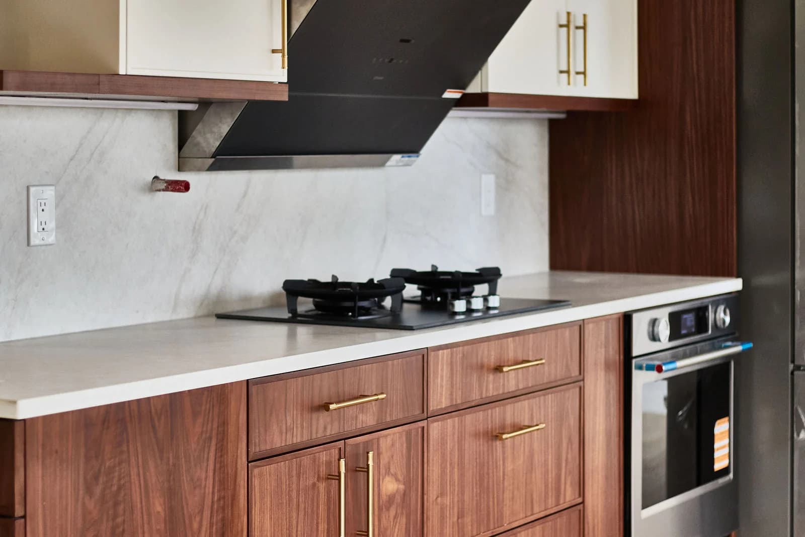 A gas cooktop sits above walnut drawers with brass pulls, beside a built-in oven. Bellevue, WA